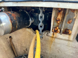 on the left, a windlass motor is rusty and covered in grime. on the right, a chainplate has dirty and rusted bolts.