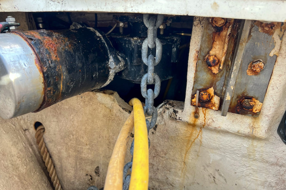 on the left, a windlass motor is rusty and covered in grime. on the right, a chainplate has dirty and rusted bolts.