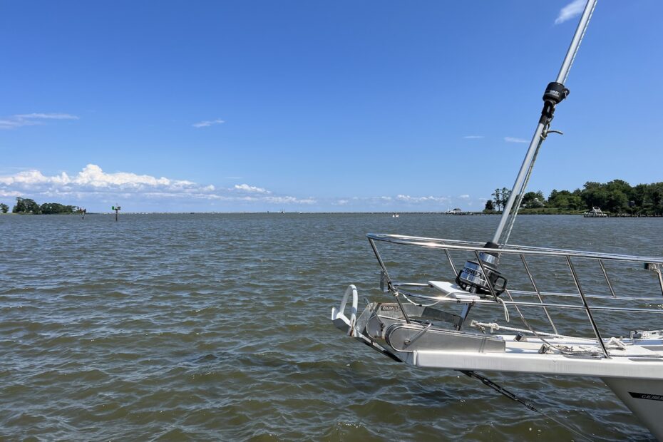 view of the chesapeake bay from a dock. sky is blue with fluffy white clouds afar. the water is a greenish brownish color, and is ripply. the bow sprit of loka extends into the photo from the right