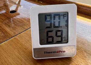 small square thermometer showing temperature, currently 90 degrees farenheit, and humidity, currently reading 69%. white thermometer is sitting on a wooden table.