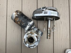 a windlass in two parts. on the left is the motor, a rusted cylinder of metal. on the right, the top of the windlass that is stainless steel and a bit shiny