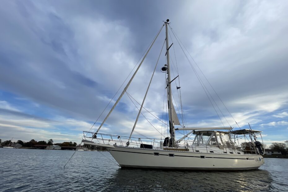 a sailboat at anchor in a large creek with trees in the background, with blue skies and grey clouds above