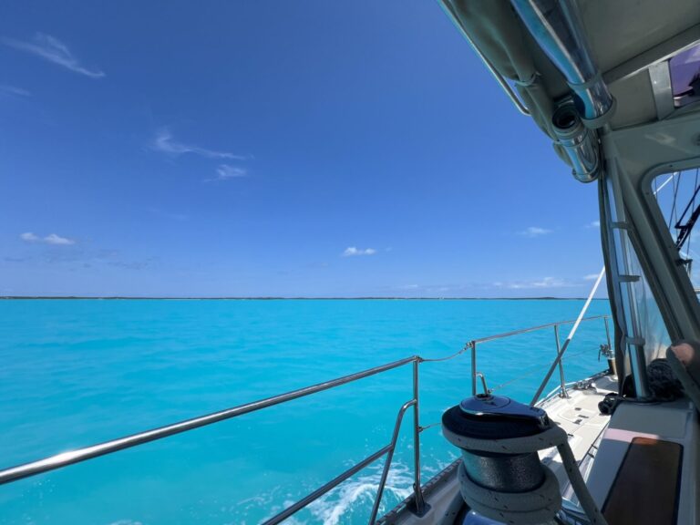 looking out from the cockpit of a sailboat at a flat, turquoise blue water under a clear blue sky
