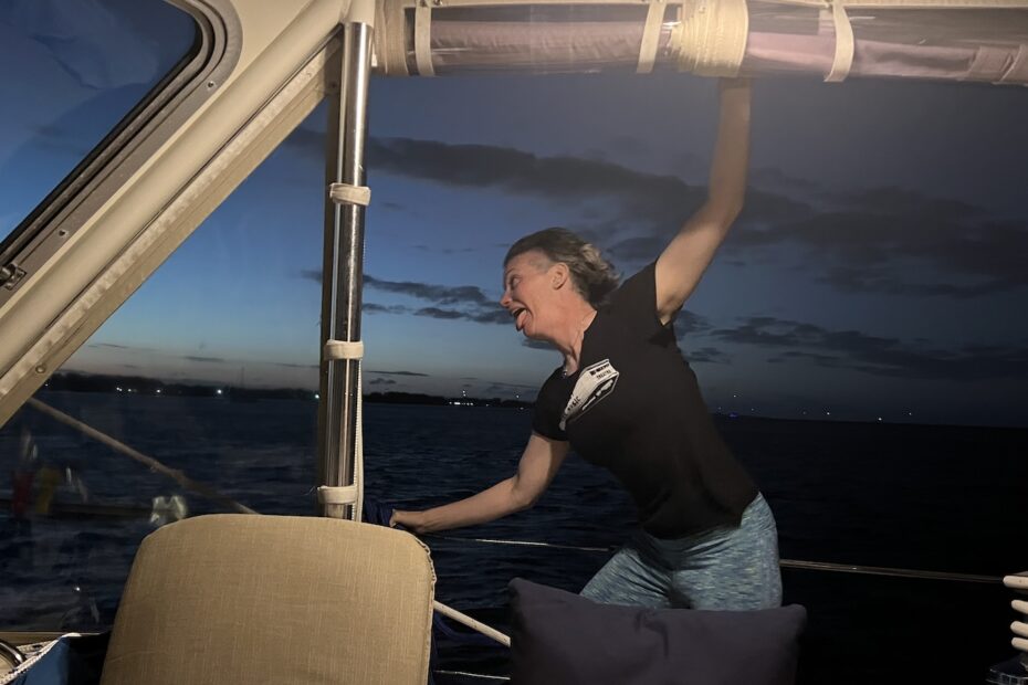 as evening is setting in, photo from inside the sailboat cockpit looking starboard at pinky, appearing to be holding on for dear life while the wind whips wildly around her.
