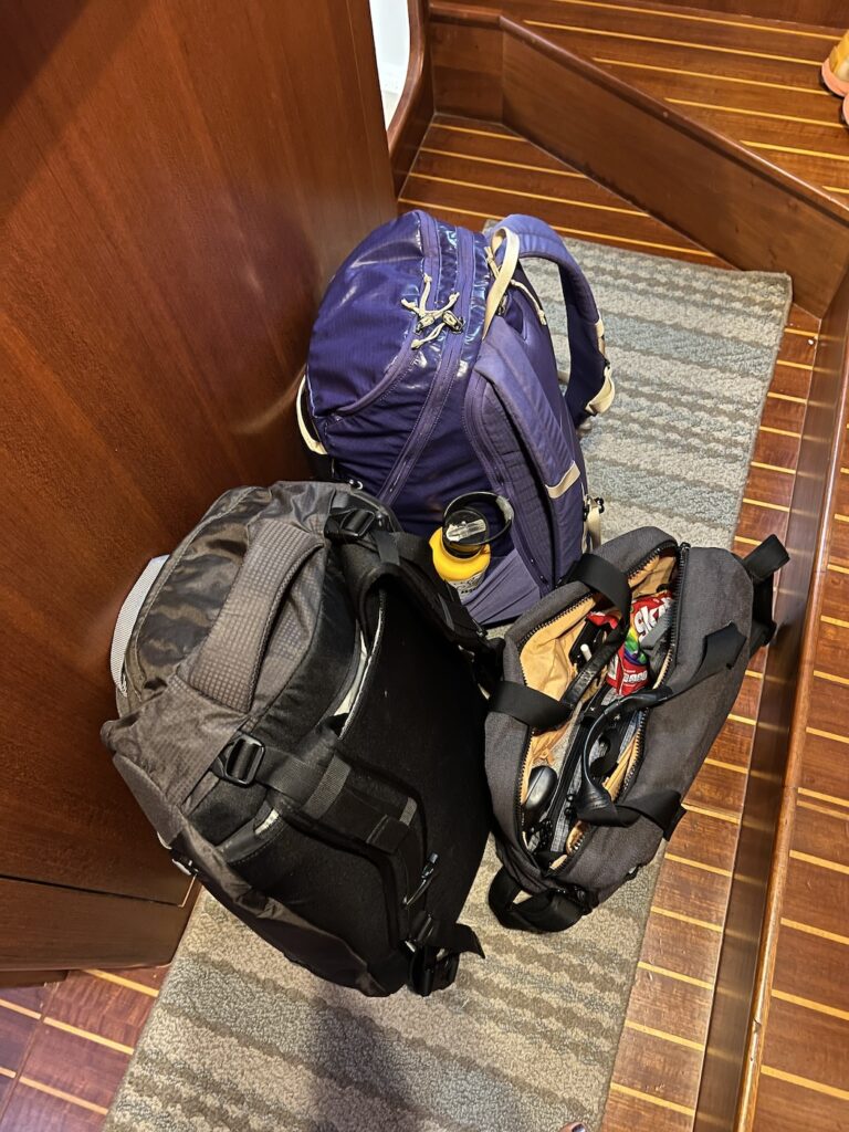 a view of 2 large backpacks packed and sitting on the floor of a home. a laptop bag also leans against the bags