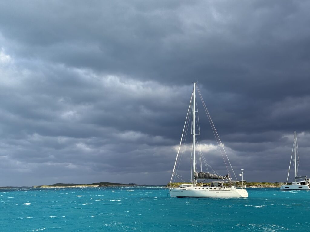 a sailboat anchored in very stormy, turqoise waters with white caps and storm clouds overhead