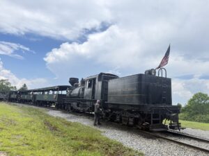 a black train with a couple of green passenger cars behind it under a blue sky with a few white clouds. historic-shay-locomotive-cass-wv.jpg