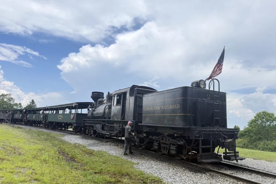 a black train with a couple of green passenger cars behind it under a blue sky with a few white clouds. historic-shay-locomotive-cass-wv.jpg